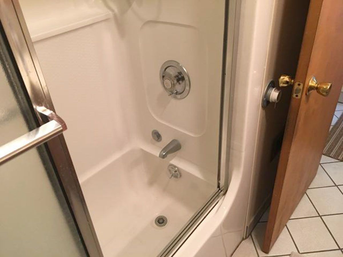 Small white shower stall with glass door, chrome fixtures, and a wooden door beside it