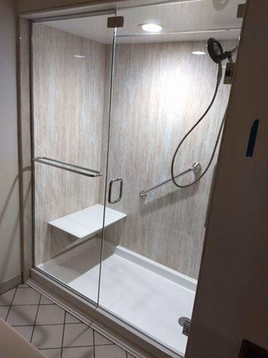 Accessible shower with a seat, glass doors, and grab bar, with beige tile walls and white floor