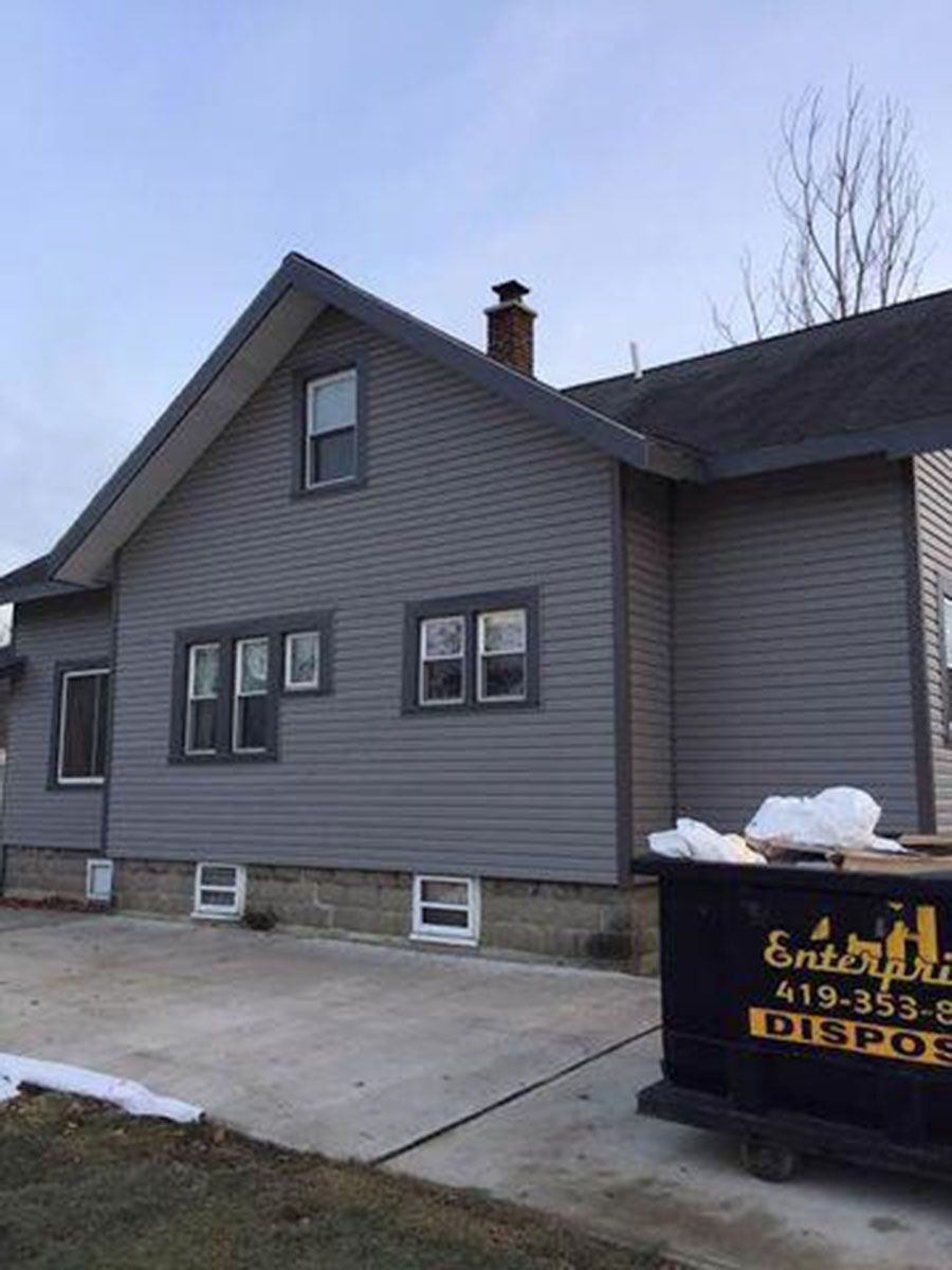 Gray-sided house with dark trim, visible windows, and a chimney