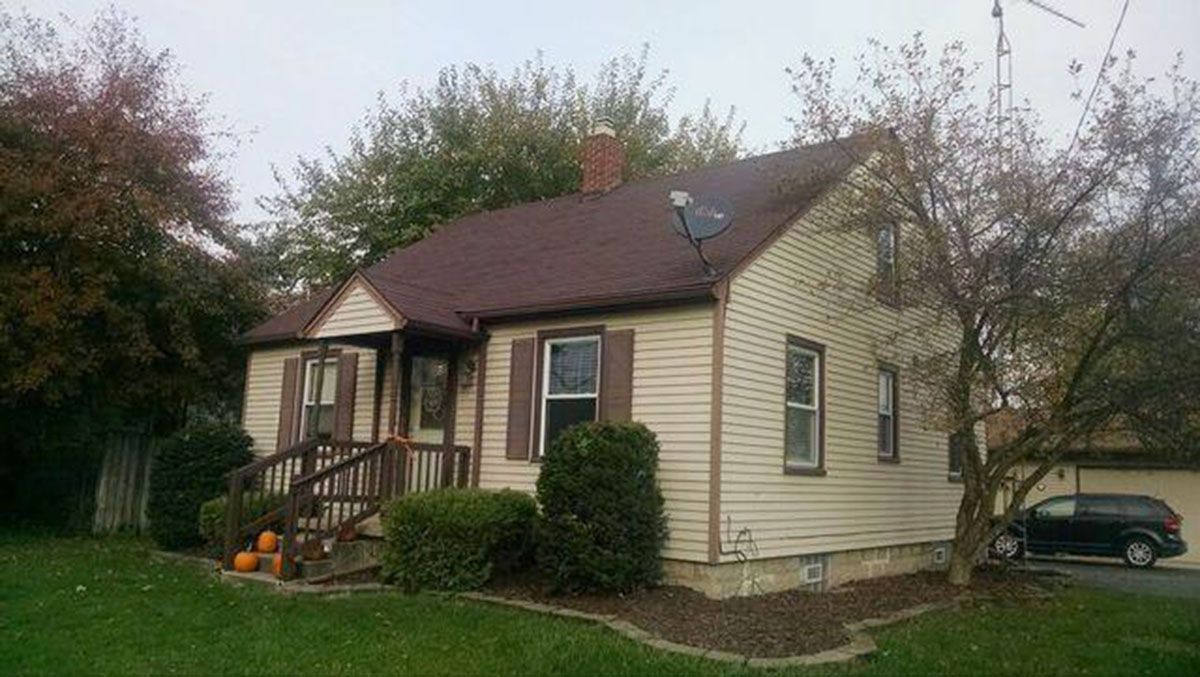 A two-story beige house with brown roof, shutters and trim
