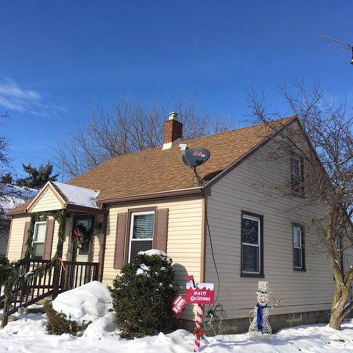 Tan house with snow, Christmas decorations, and a clear blue sky