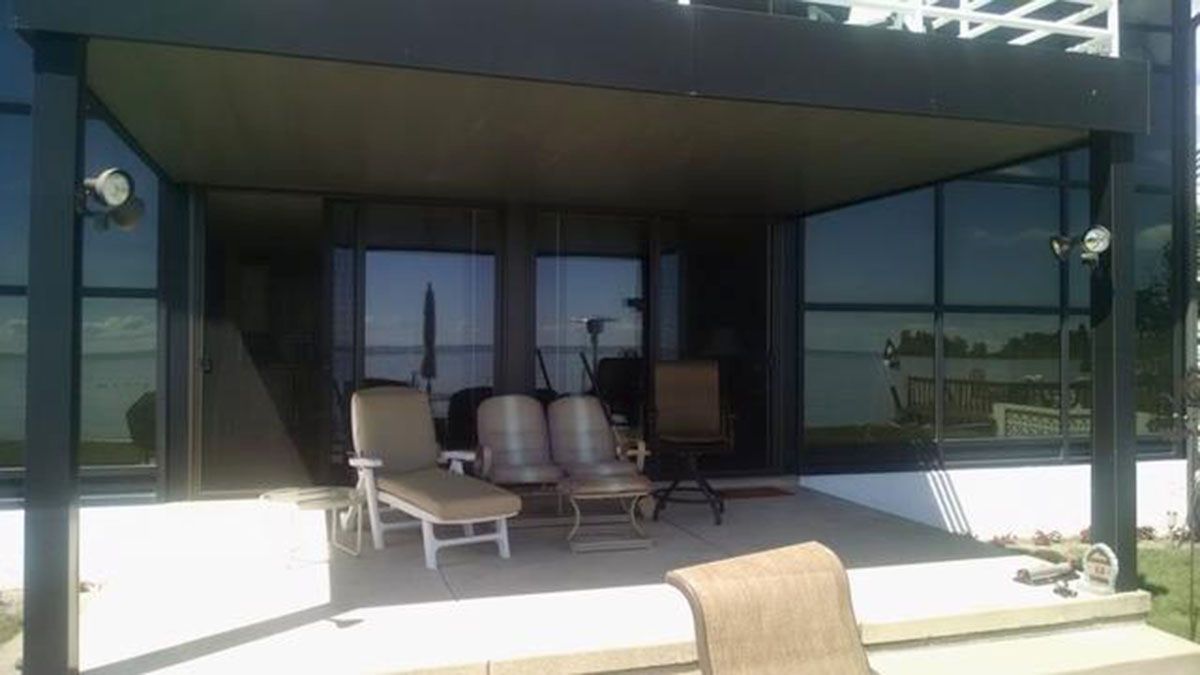 Covered patio with seating overlooking a body of water through glass windows