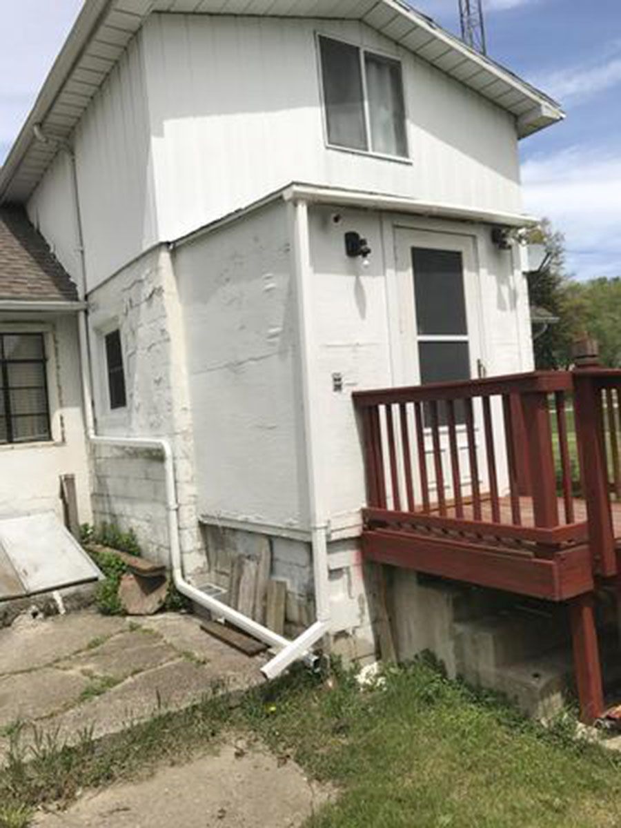 Exterior of a white two-story building with a small deck and a white gutter; partial concrete foundation visible