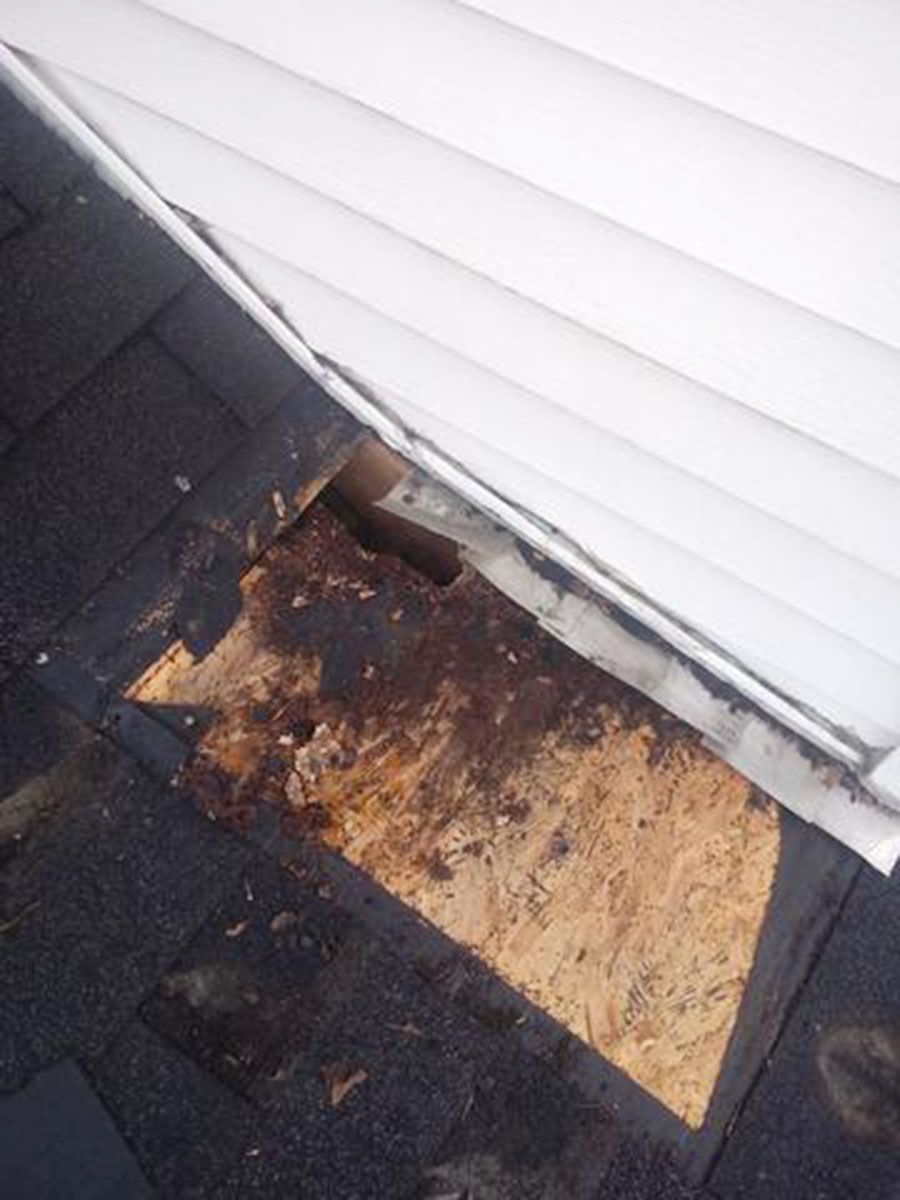 Damaged roof section with exposed wood beneath white siding
