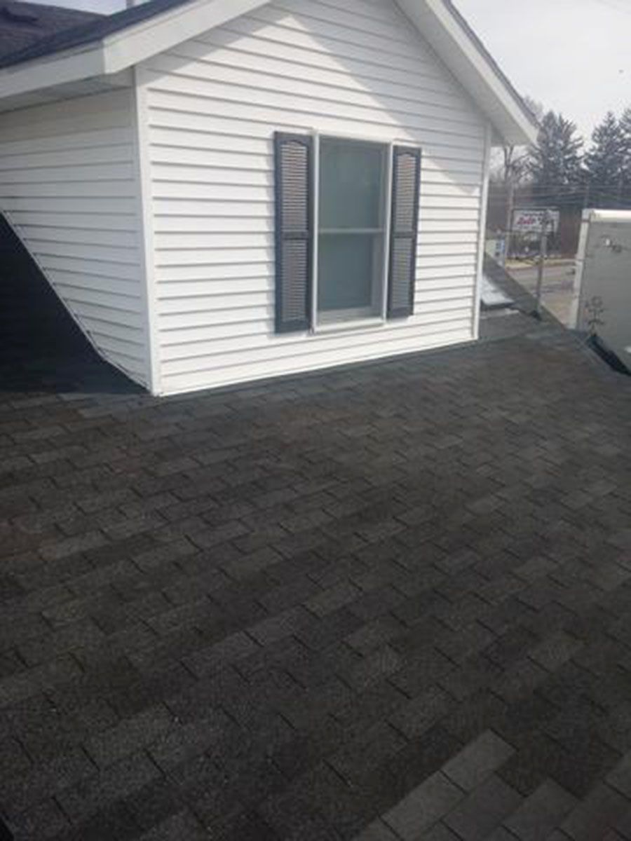 White building with gray shingled roof, window with black shutters