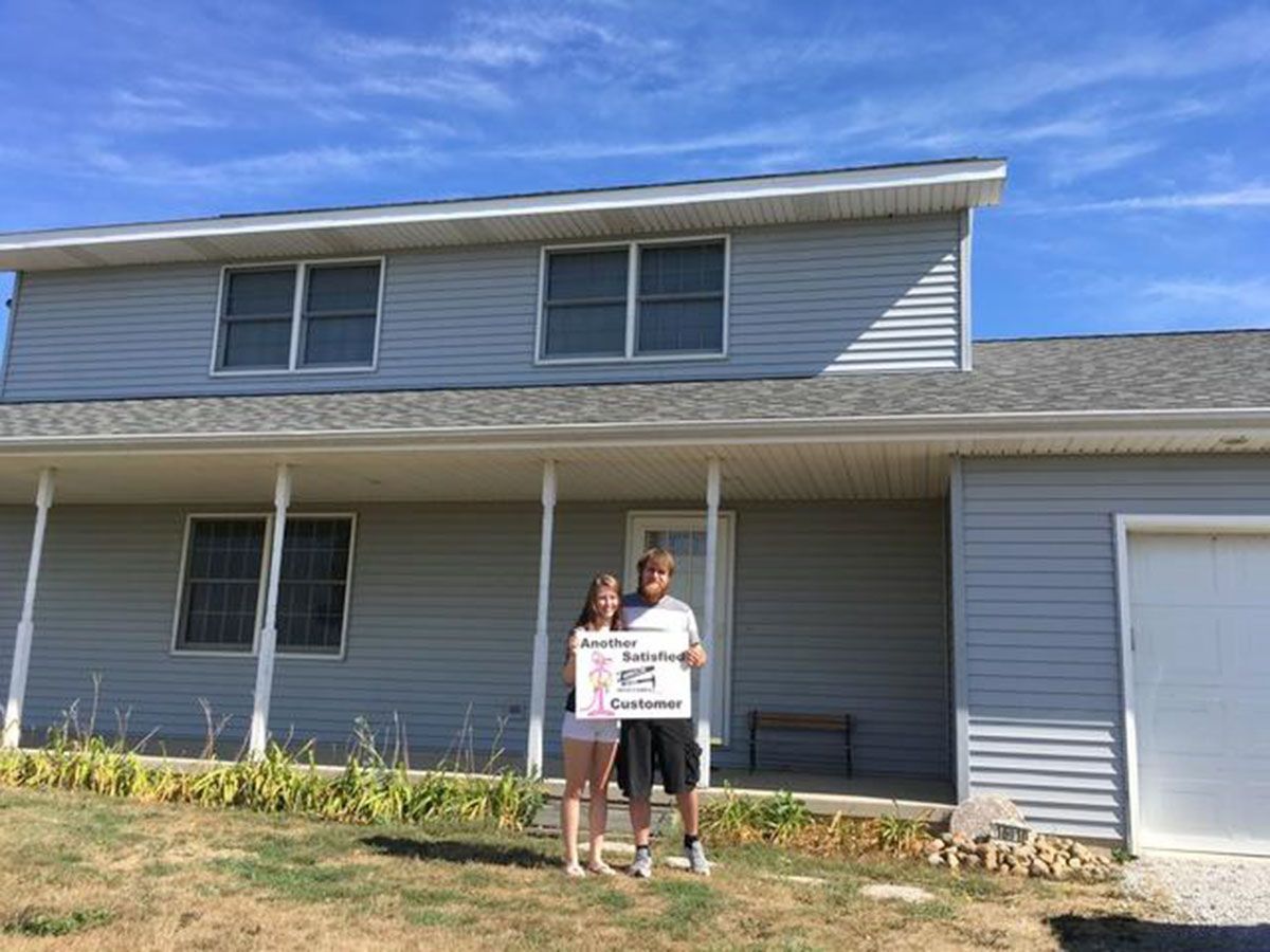 Couple holding sign in front of a blue two-story house