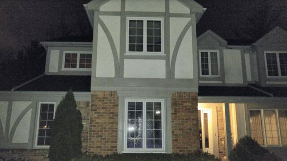Two-story house at night with white and brown exterior, arched features, multiple windows, and a dark roof