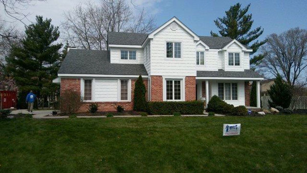 Two-story white house with brick accents, dark roof, and lush green lawn