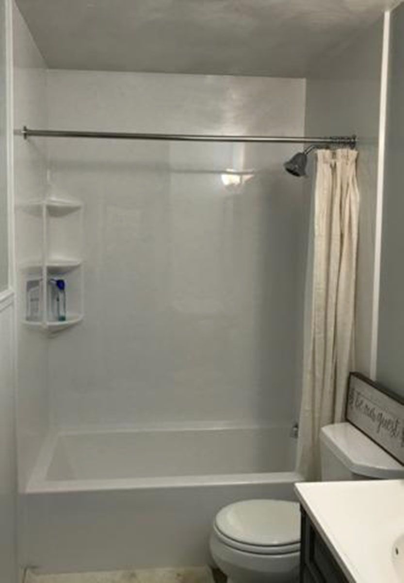 A white, built-in bathtub and shower with a curtain and a shelving unit in a bathroom