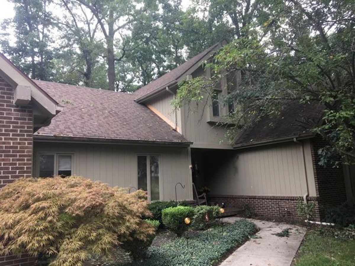 House exterior with brick and siding, brown roof, and lush green landscaping