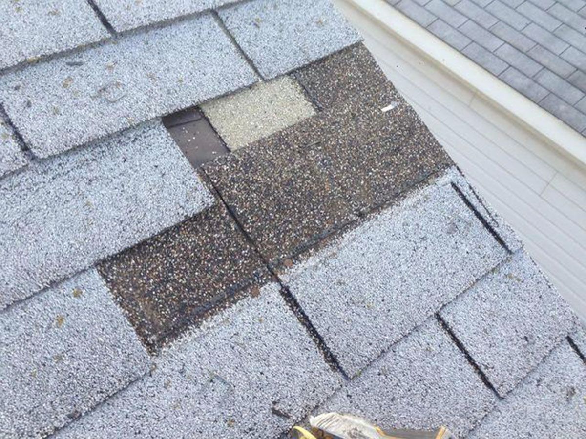 Damaged asphalt roof shingles with missing and discolored patches, near a white gutter