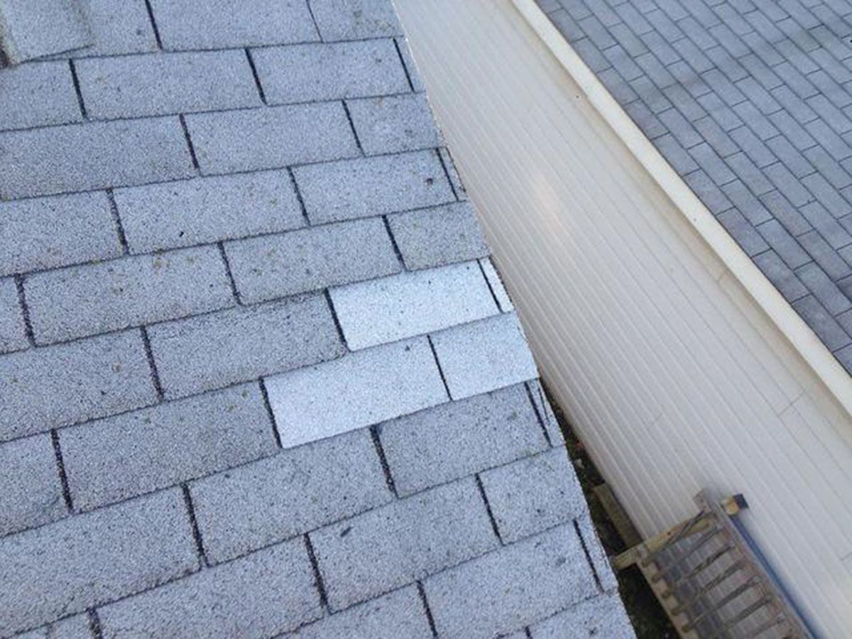 Gray asphalt shingles on a roof with two lighter colored replacements next to a white siding wall