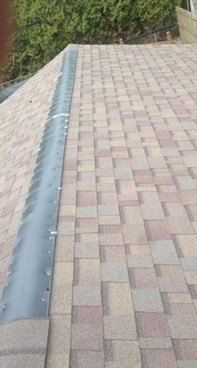 Close-up of a roof ridge with black flashing installed over brown and tan asphalt shingles