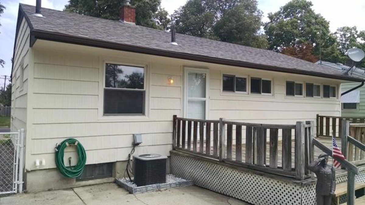 Back of a beige house with a brown roof, windows, and a deck