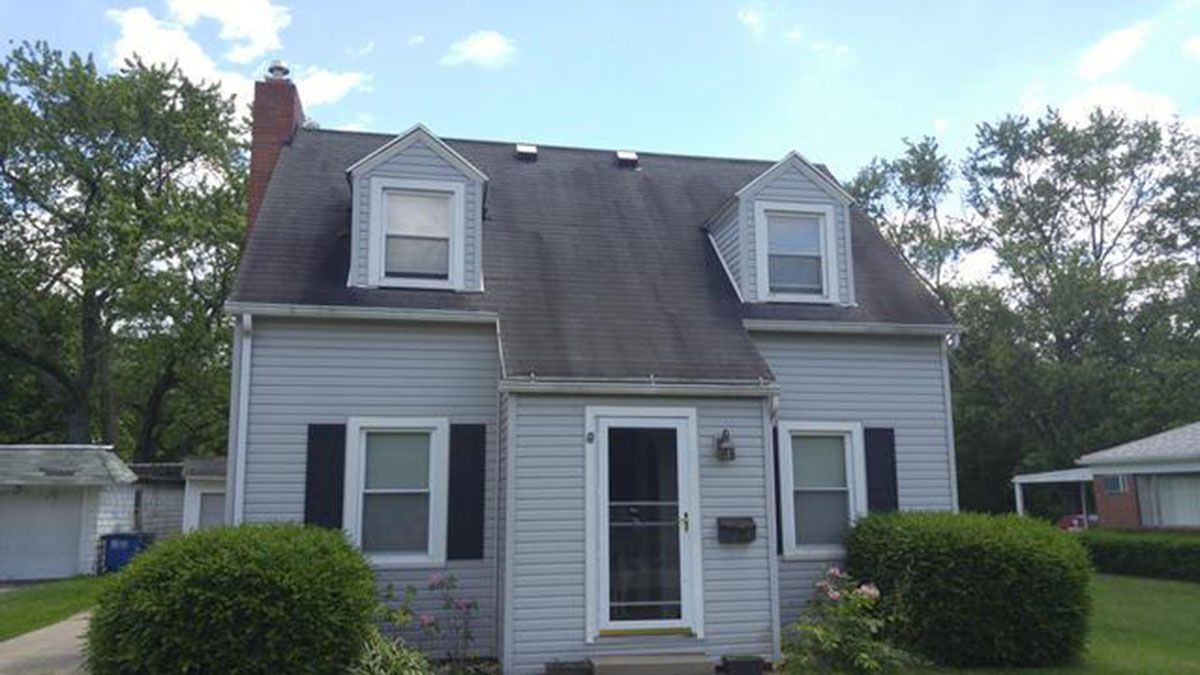 Gray house with black shutters, two dormers, and a chimney on a sunny day