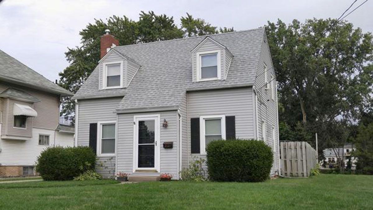 Gray two-story house with dormers, black shutters, white door, and a green lawn