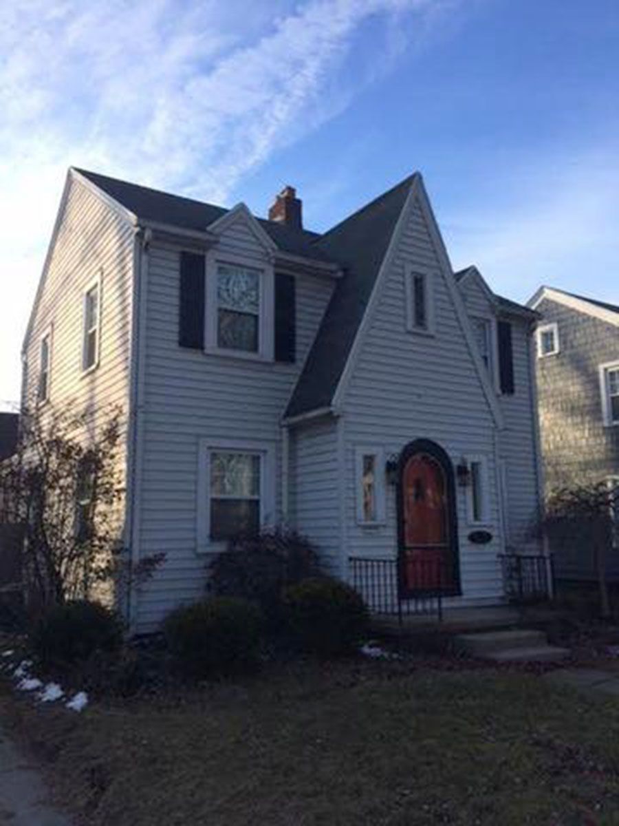 Two-story white house with black shutters, a dark roof, and a red door under a clear blue sky