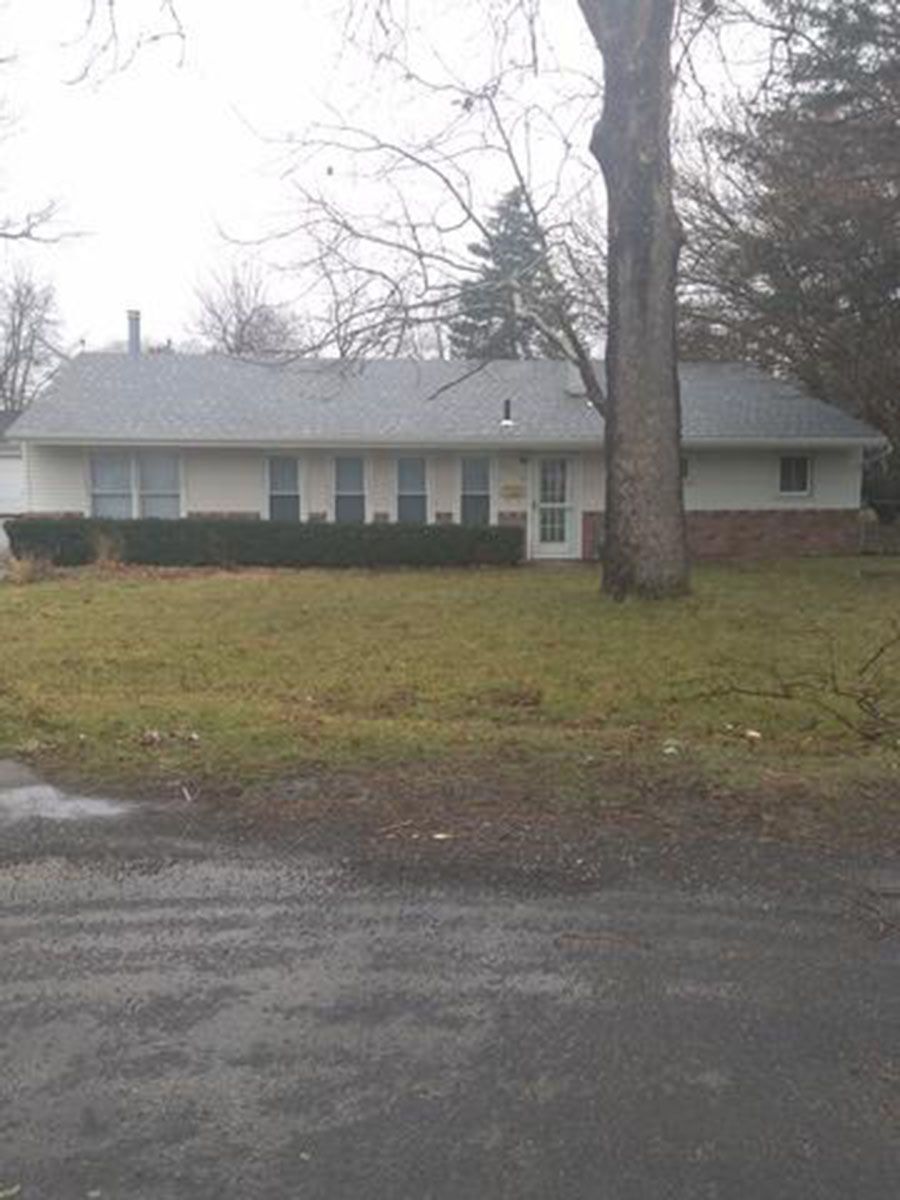 Single-story light-colored house with a dark roof and leafless tree in the front yard