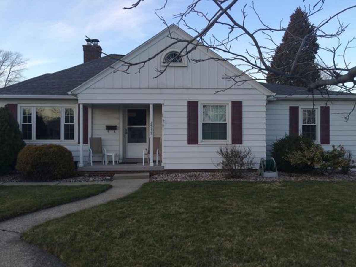 White house with dark red shutters and a small front porch, gray brick chimney, and a pathway to the door