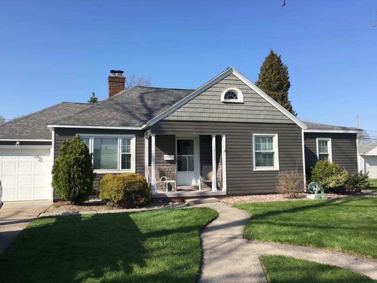 A one-story house with gray siding, white trim, and a concrete path leading to the front door
