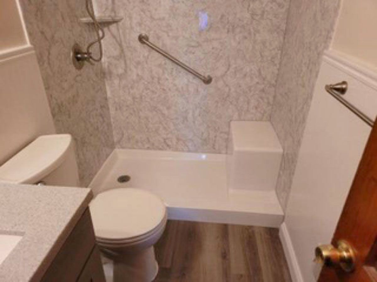 Accessible bathroom with a walk-in shower, grab bar, and built-in seat; toilet and sink visible