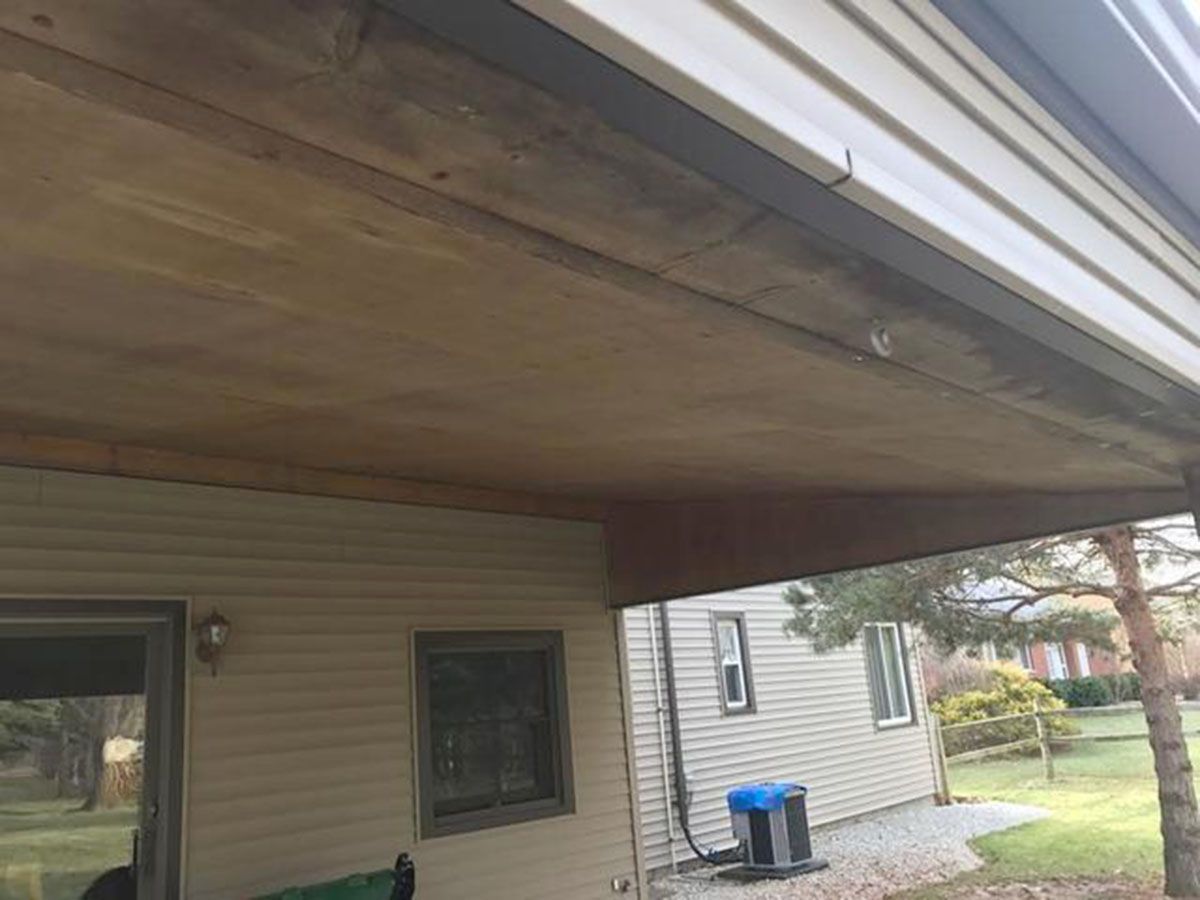 View from below of a wooden porch ceiling and vinyl siding on a house
