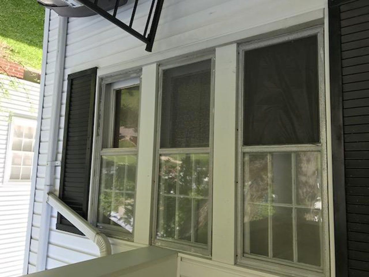 Three white-framed windows with screens on a white house exterior, a black shutter, and a black railing overhead