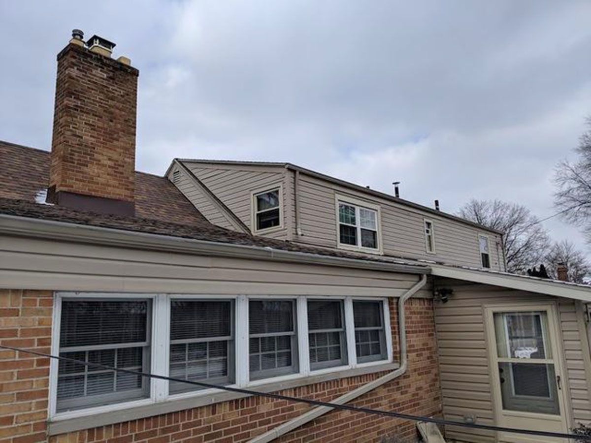 Brick house with brown roof, tan siding, and multiple windows under cloudy sky