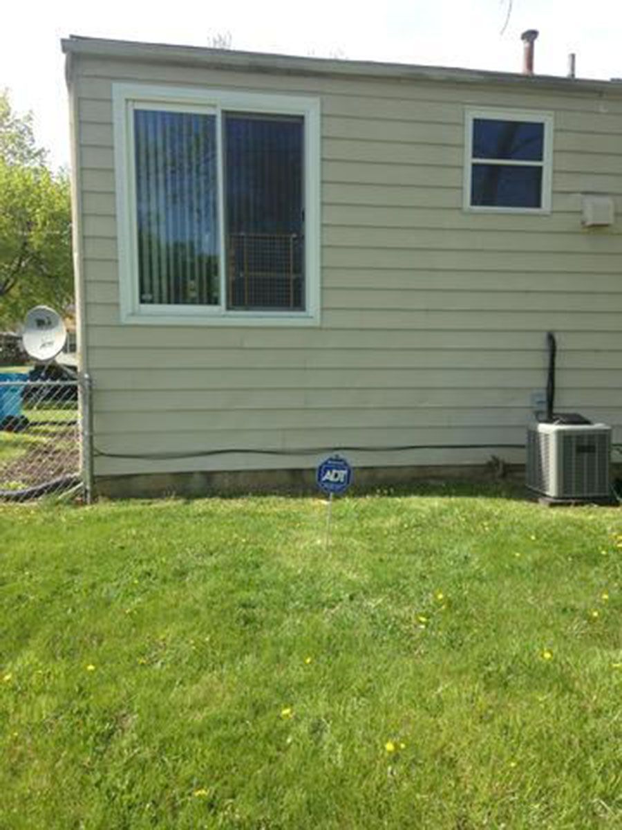 Backyard view of a beige house with a sliding glass door, small window, and green grass