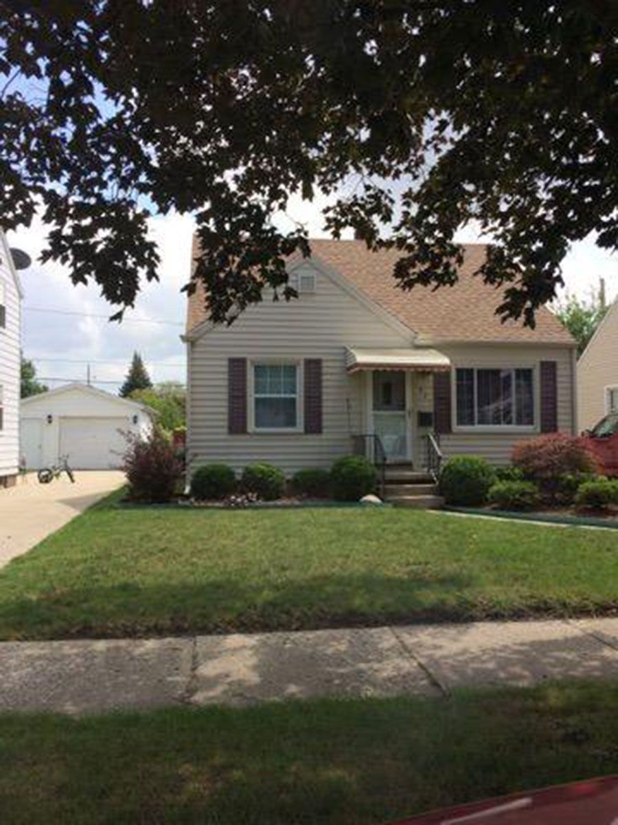 Beige house with brown shutters, small porch, and green lawn