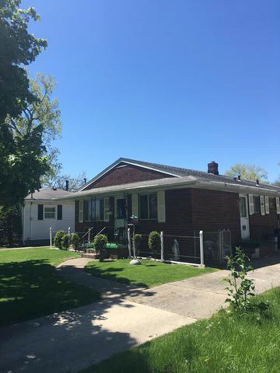 Brick and white-sided houses under a blue sky, with a sidewalk and green lawns in front