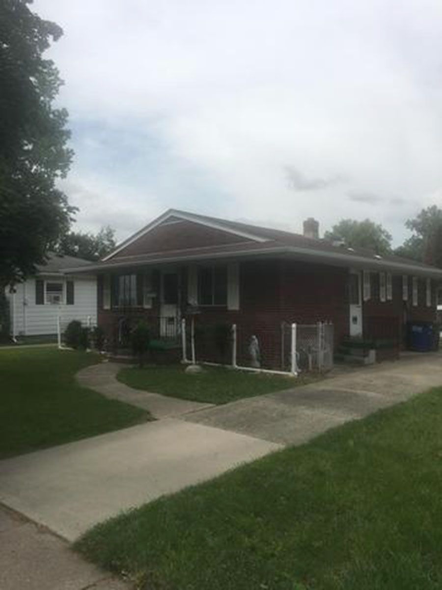Brick house with white trim, driveway, and lawn under a cloudy sky
