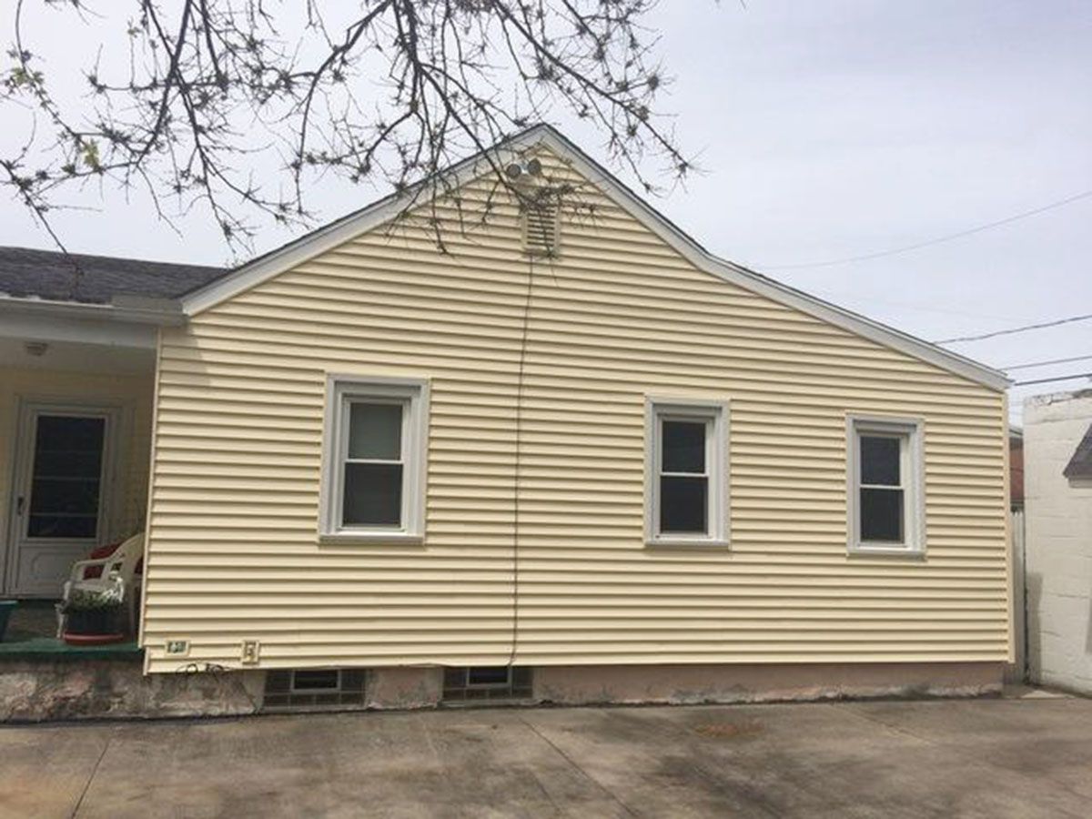 Yellow-sided house with three windows and a concrete foundation; overcast day