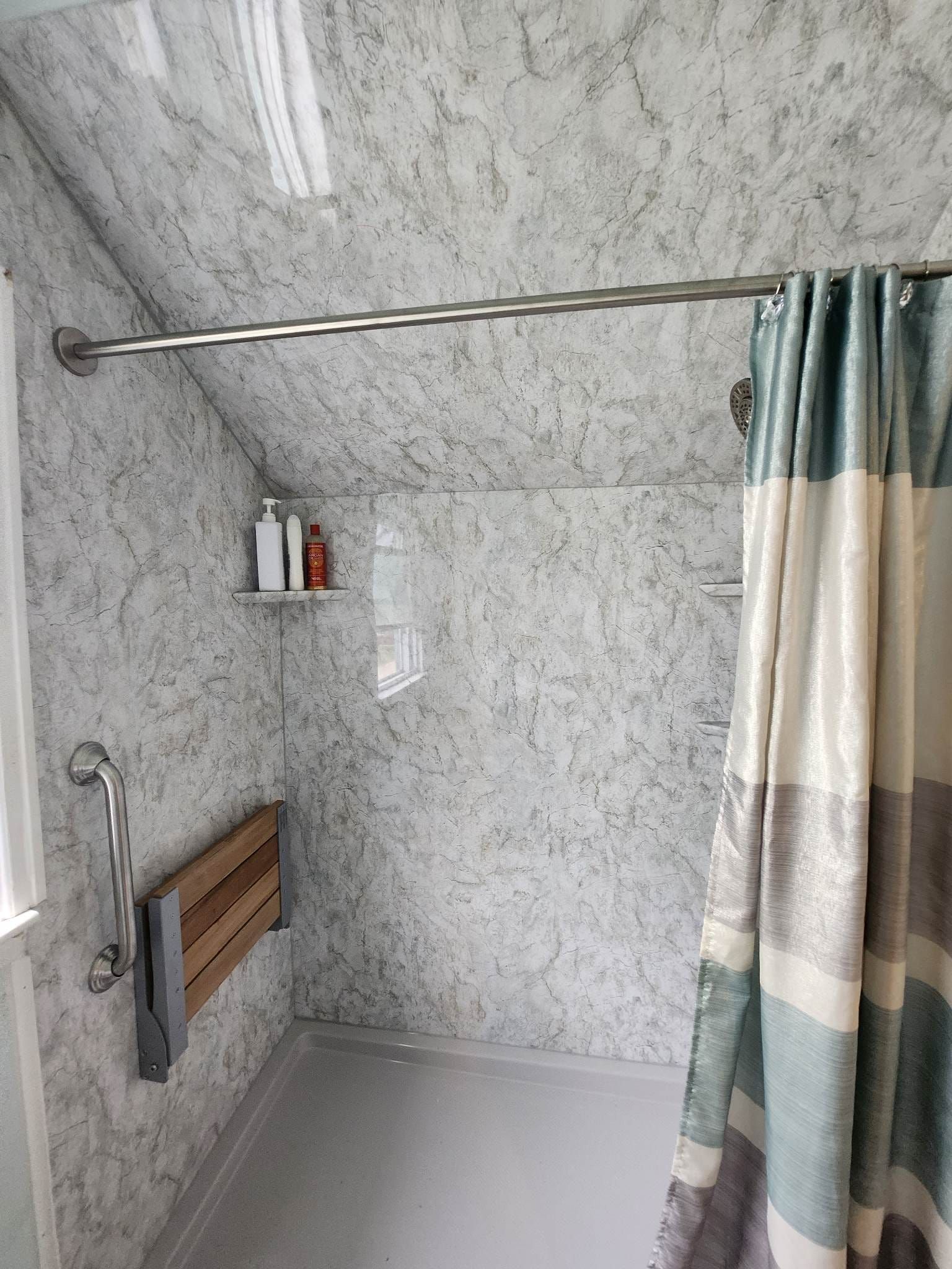 Accessible shower stall with grab bar, folding seat, and shower curtain.