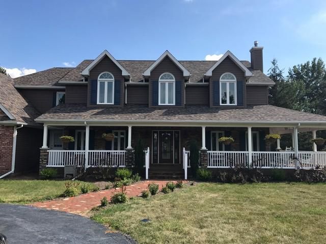 Brown house with white porch, three arched windows, and a brick walkway on a sunny day.