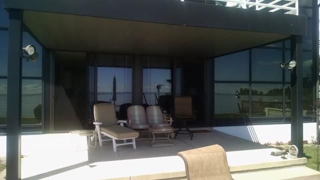 Patio with seating under a covered area; glass windows reflect the water and sky.