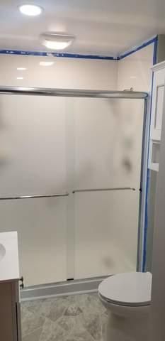 Bathroom with frosted glass shower doors, a toilet, and light fixture. Tape lines the walls.