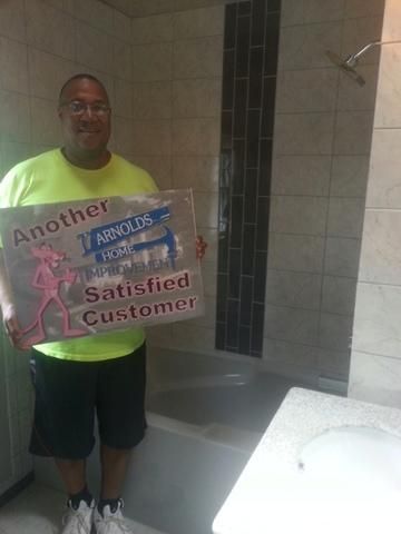 Man holding a sign in a newly renovated bathroom with a shower and vanity.