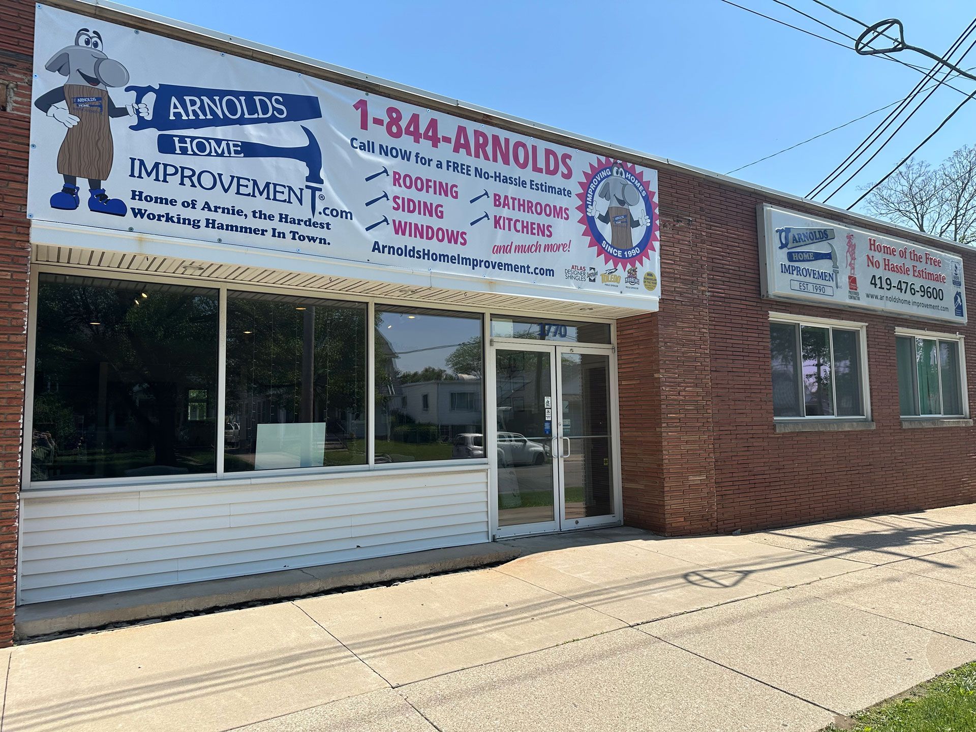 Storefront for Arnold's Improvement, a brick building with white awning and large windows under a bright sky
