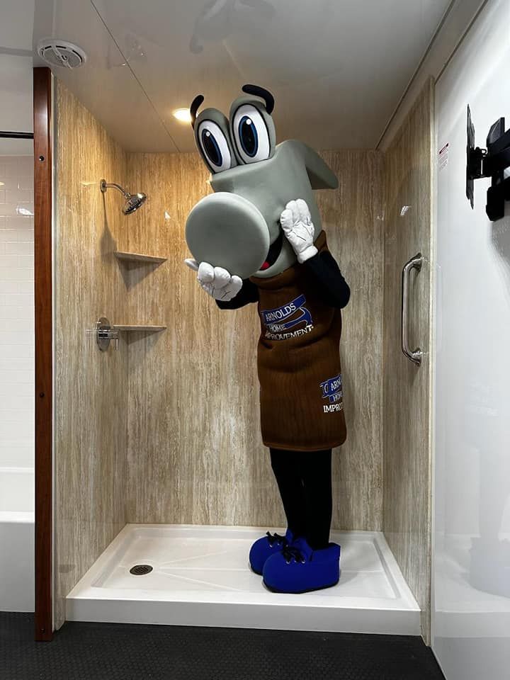 Person in a shower stall with a large cartoon animal mask, wearing a brown outfit and blue shoes.