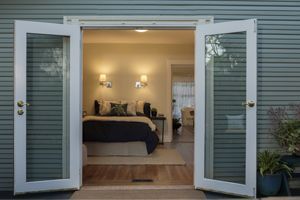 Open French doors into a warmly lit bedroom with a dark bed and bedside lamps.