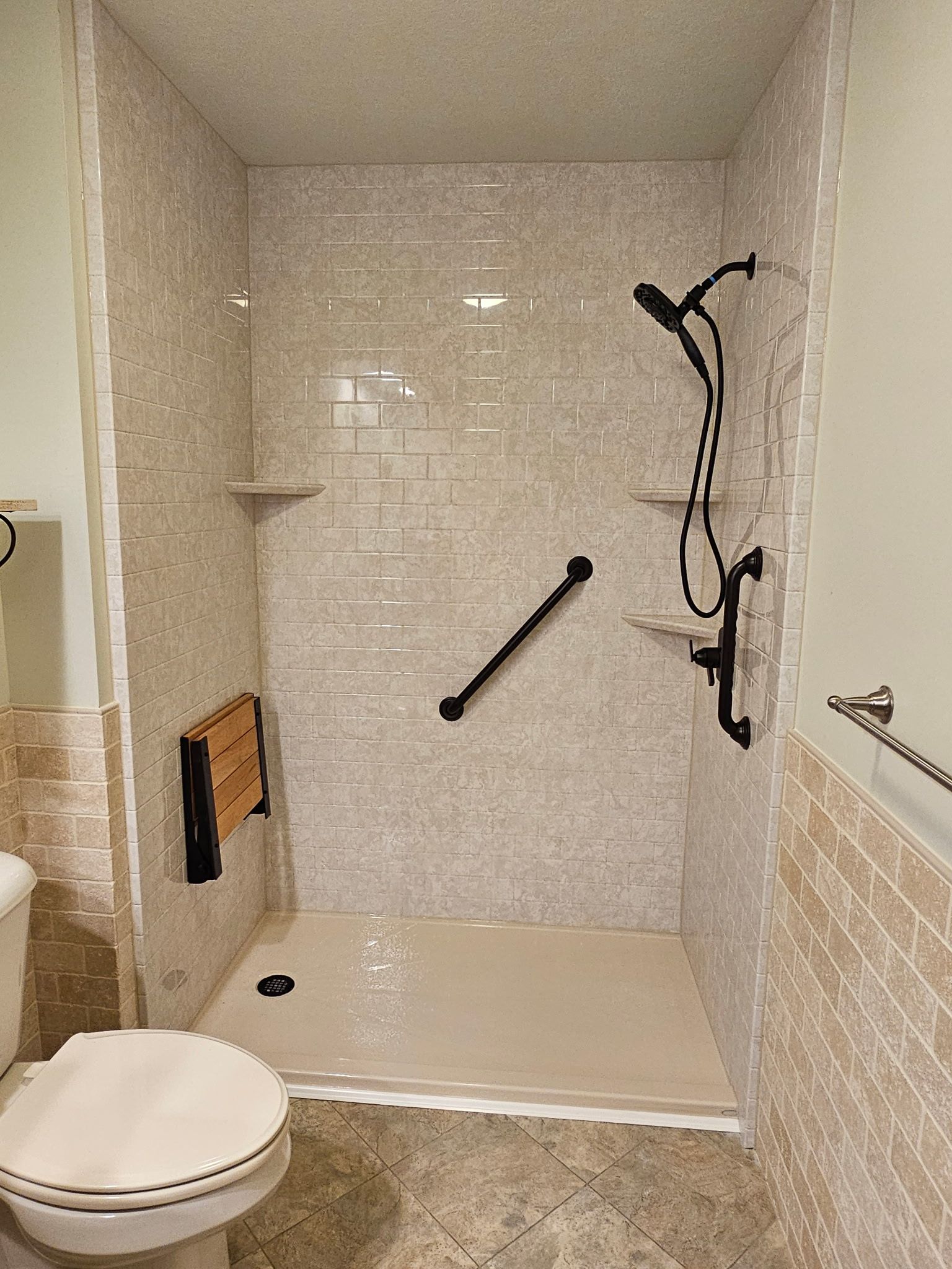 Bathroom with a walk-in shower, white tile, grab bars, and a shower seat.