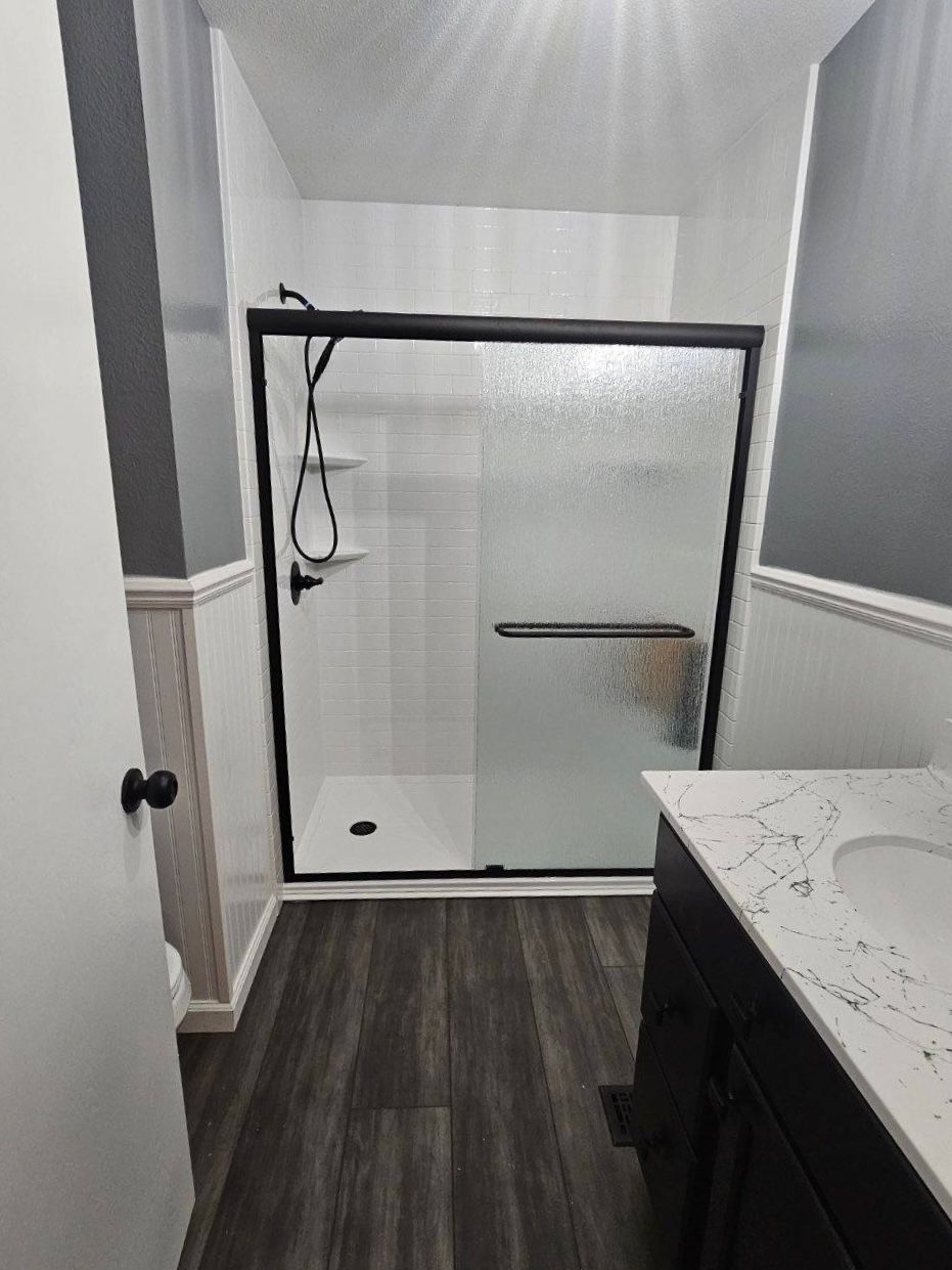 Bathroom with a glass shower enclosure, gray walls, and dark wood flooring.