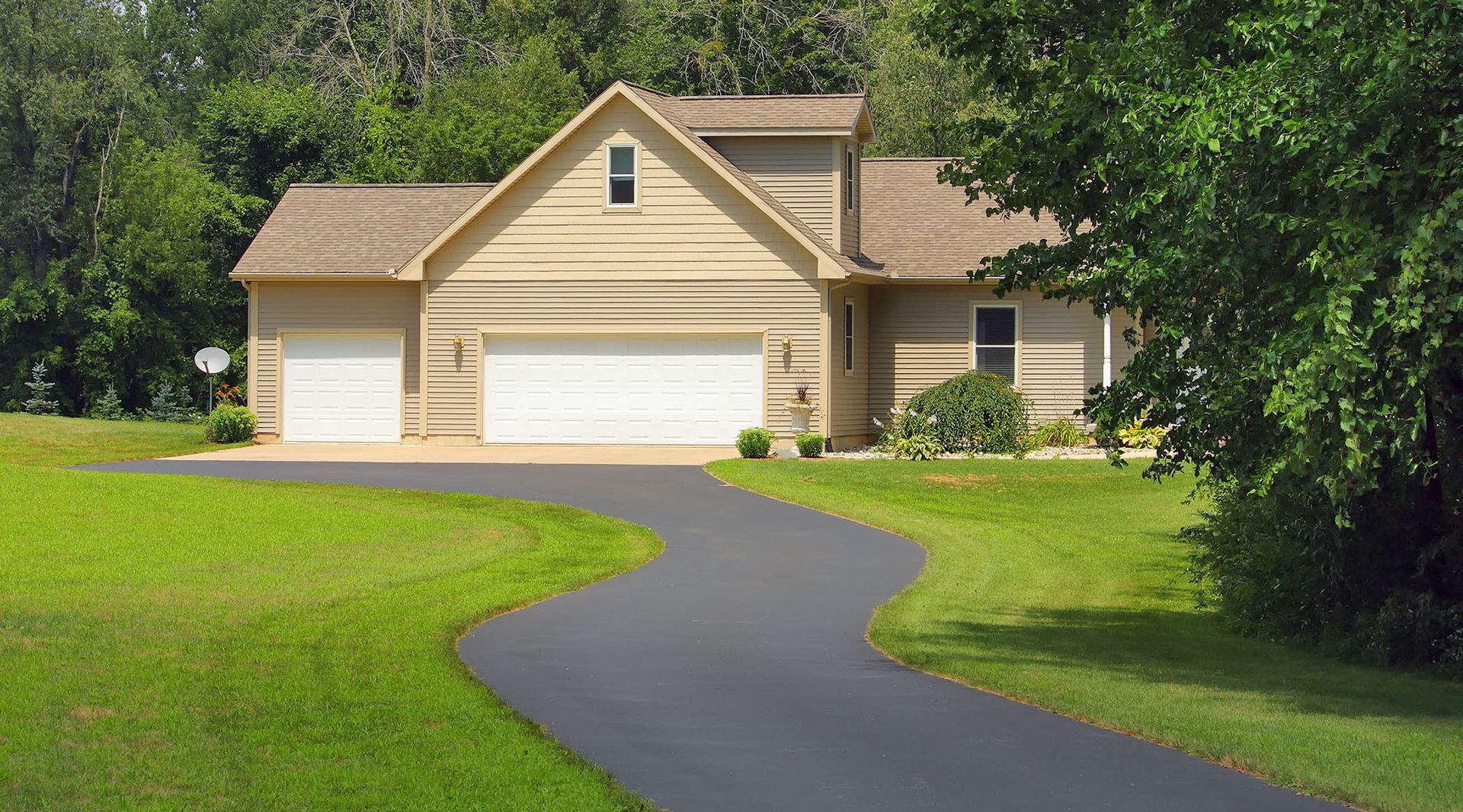 A tan, single-story house with a two-car garage and a smaller side garage sits at the end of a winding asphalt driveway.