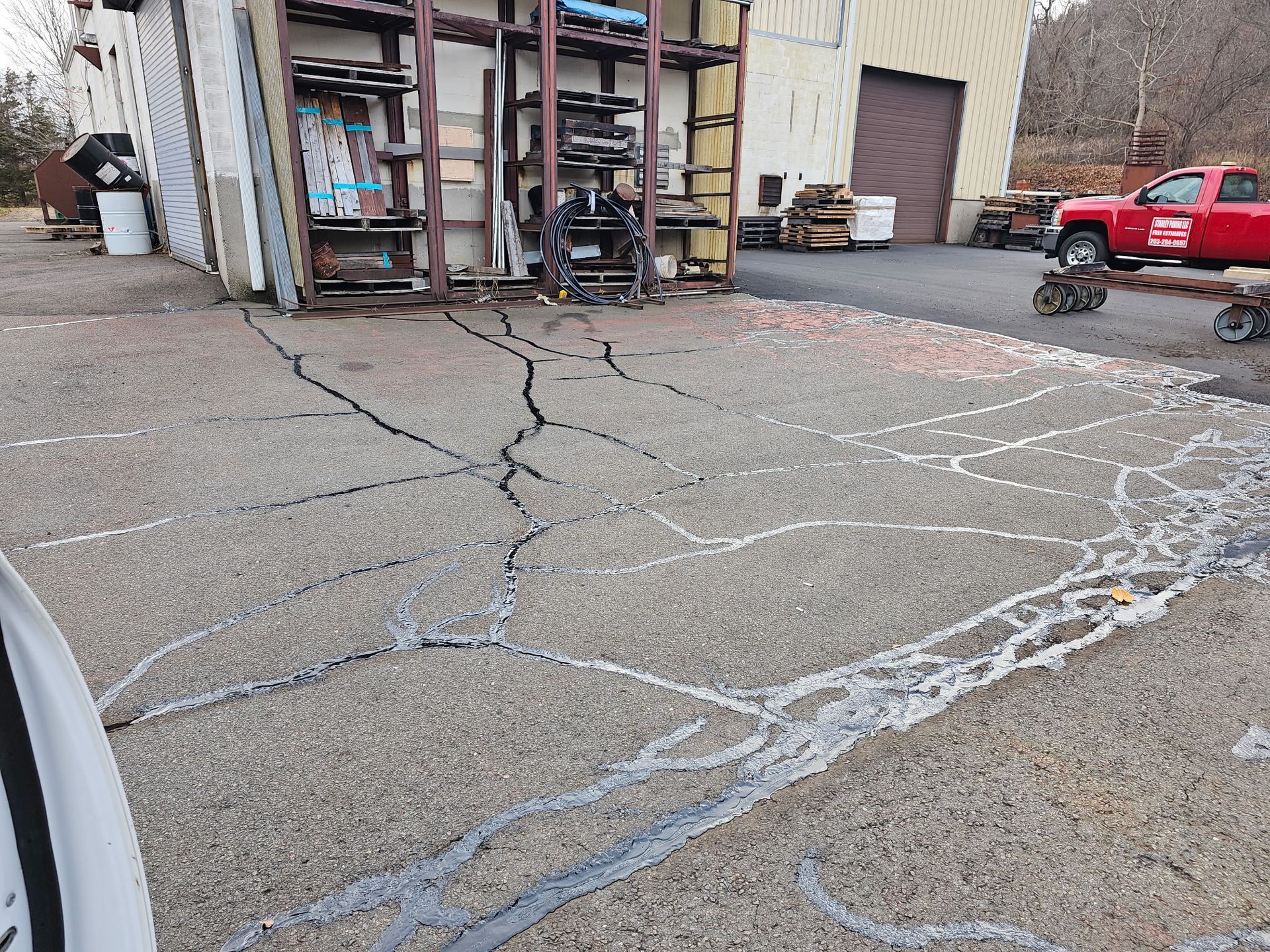 Cracked asphalt parking lot surface with gray crack-filler sealant applied in a branching pattern.