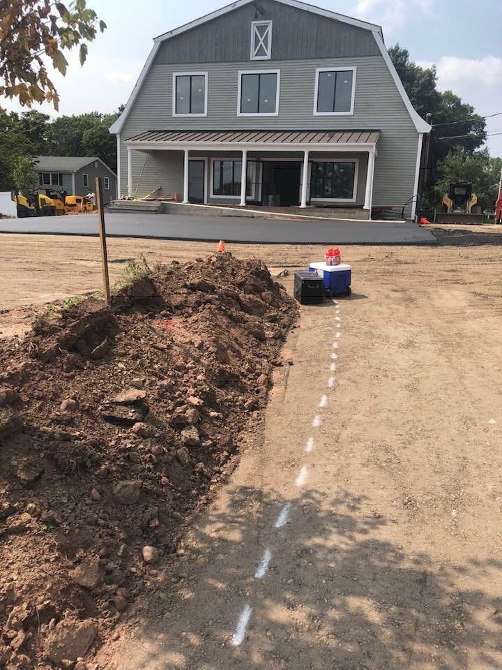 A large, gambrel-roofed barn building with a new concrete patio, next to a trench and a line marked on the ground.