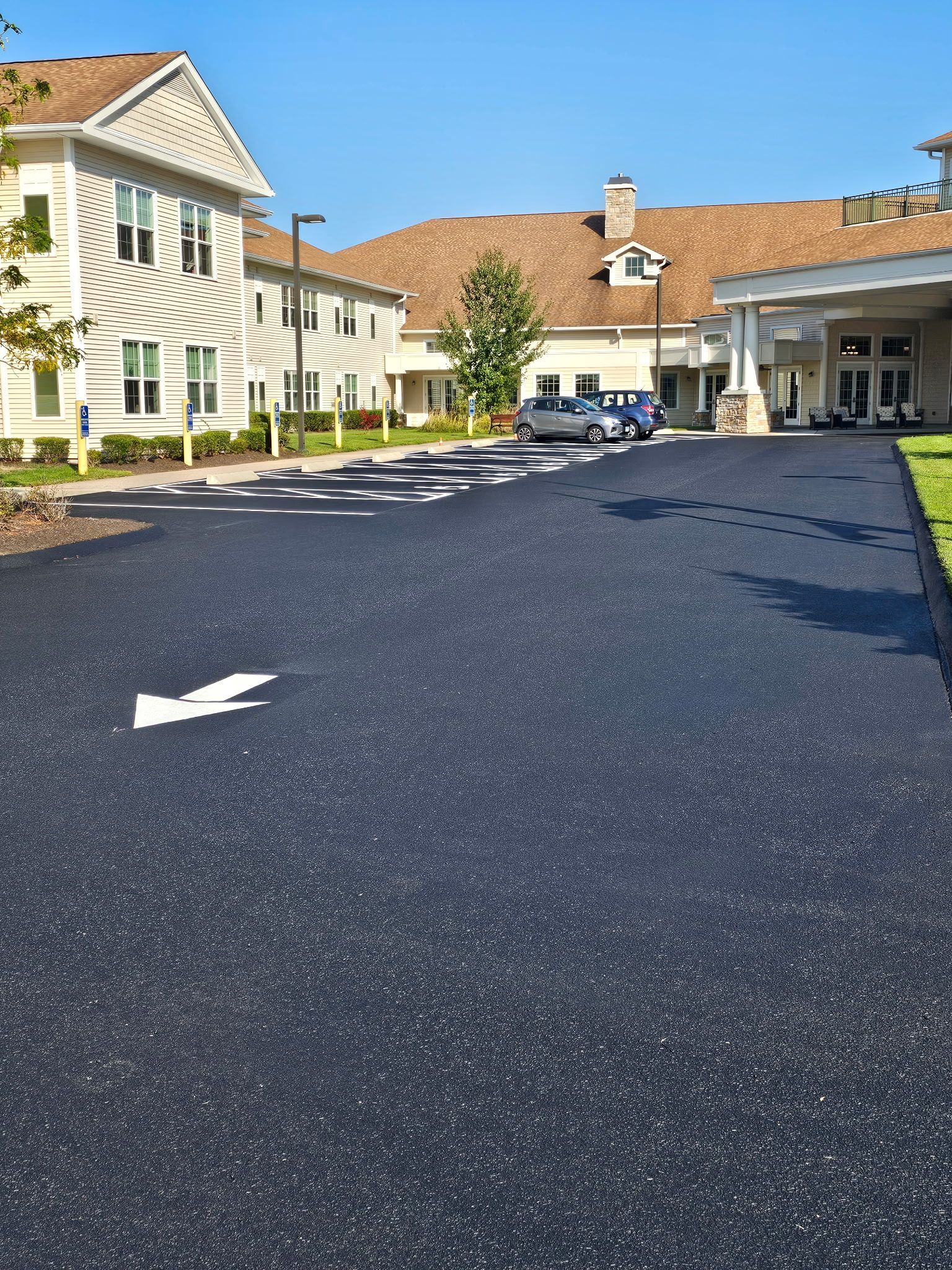A freshly paved black parking lot with white directional arrows, situated in front of a multi-story residential building.