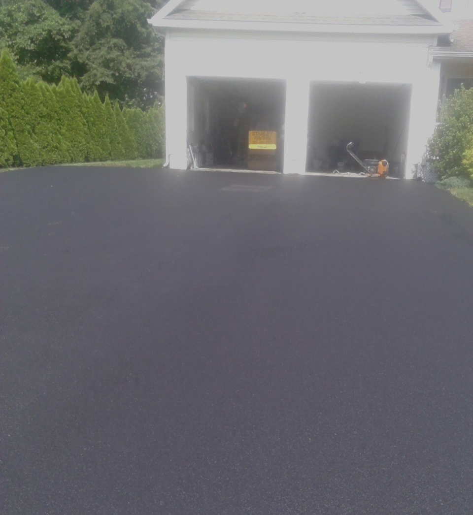 A freshly paved black asphalt driveway leads to a two-car garage at the base of a white house.