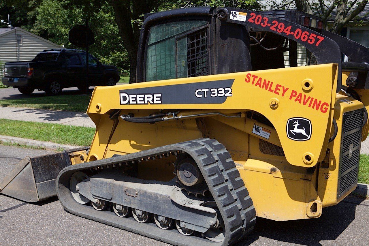 A yellow John Deere CT 332 tracked skid steer loader for Stanley Paving parked on an asphalt street.