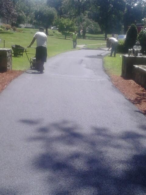 Three workers apply fresh black asphalt to a residential driveway on a sunny day.
